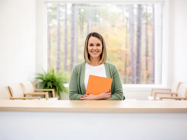 A clinic office manager holding a folder behind a reception counter.